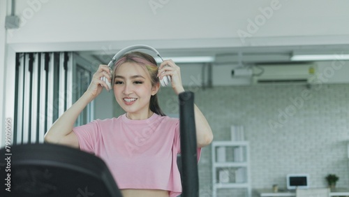 Young Asian woman wearing headphones exercising on treadmill at gym