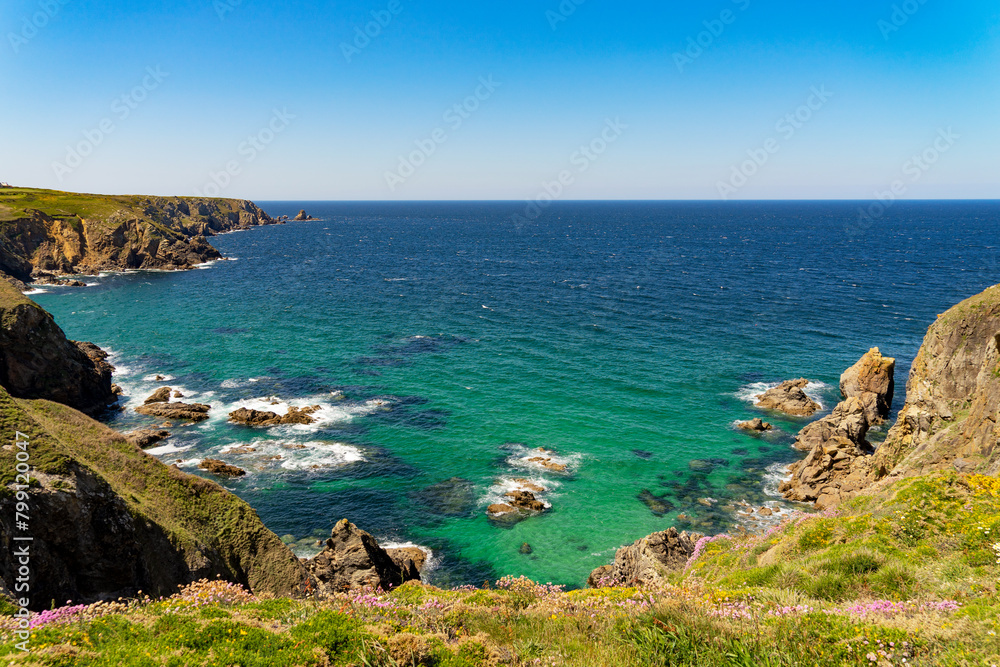 Vue sur les falaises et les eaux turquoise de la mer d'Iroise, sous un ciel bleu, au printemps sur la côte sauvage du Finistère, avec des arméries maritimes en fleur.