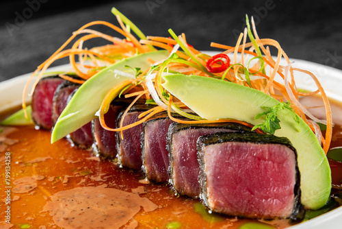 Exquisite gourmet dish featuring seared tuna slices, fresh avocado, and vibrant garnish, served in a savory sauce. photo