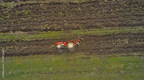 A tractor lying on its side in a plowed field, captured from above with a drone for aerial photography. The tired tractor takes a rest after its work, lying on its side.