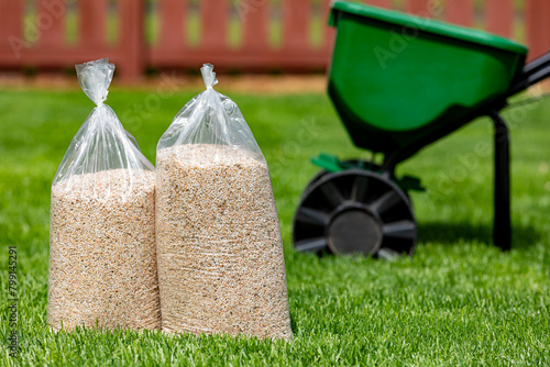 Bags of lawn fertilizer and herbicide with broadcast spreader in yard with healthy grass. Lawn care, weed control and landscaping concept. photo