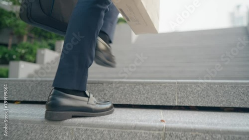 Following low angle shot of business man walking up the stairs, travel for morning city commute to office, walking up the stairs. Holding bags and working briefcase hand full of stuff going to work