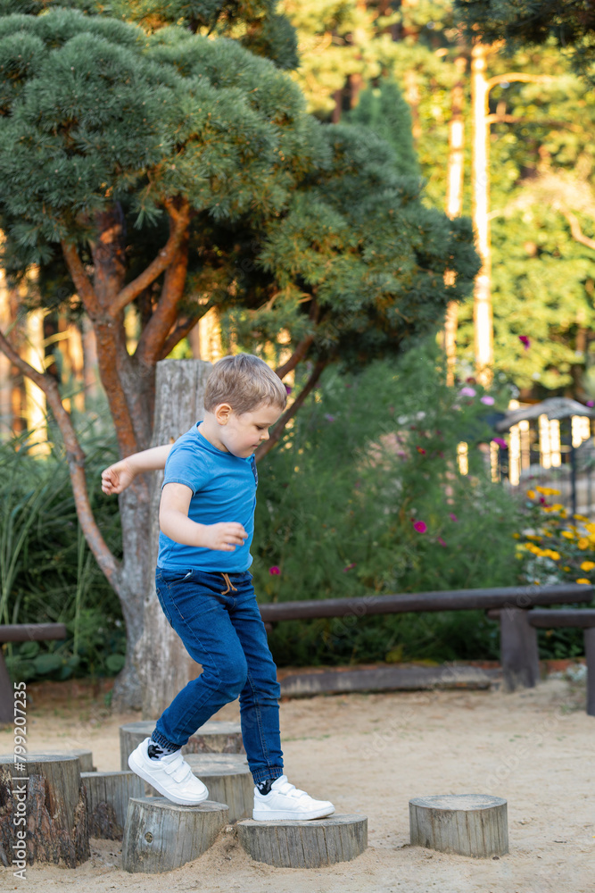 A little boy is walking on a stump obstacle course in the playground. Concept: Free time in the fresh air on the weekend A little boy is walking on a stump obstacle course in the playground. Concept: Free time in the fresh air on the weekend