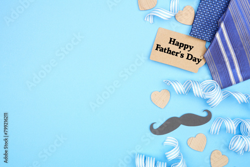Happy Fathers Day gift tag with side border of gifts, decor, ties and ribbon. Top down view on a blue background. Copy space.