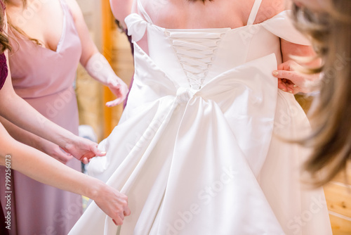 Bridesmaids are adjusting the back of a plus sized bride's wedding dress and the bow at the back of the dress during the getting ready part of the day.