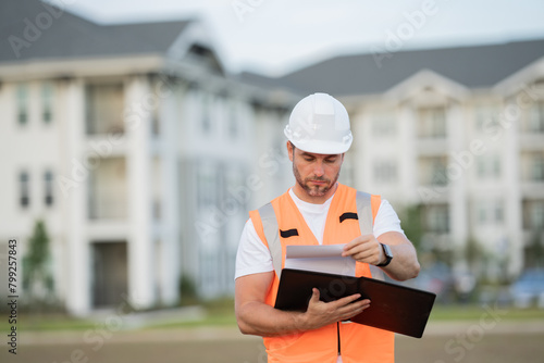 construction inspector in a helmet and construction vest with a clipboard and tablet. male worker at a construction site looking at construction drawings of a new building. 