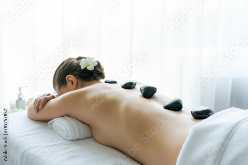Hot stone massage at spa salon in luxury resort with day light serenity ambient  blissful woman customer enjoying spa basalt stone massage glide over body with soothing warmth. Quiescent