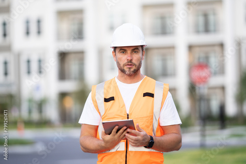 construction inspector in a helmet and construction vest with a clipboard and tablet. male worker at a construction site looking at construction drawings of a new building. 