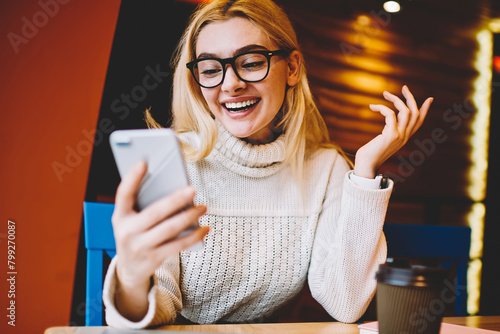 Cheerful hipster girl excited with good news reading mail on smartphone sitting in coffee shop, emotional woman happy about getting discount for internet communication checking news on telephone