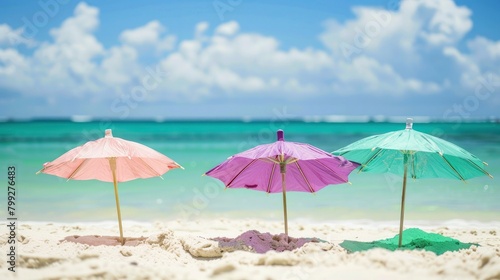 3 green, pink and purple cocktail umbrellas on the beach with white sand, ocean in the background.