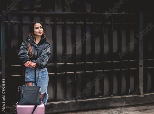 Stylish travel and urban exploration: vibrant young latina brunette with fashion look and pink suitcase exploring city downtown