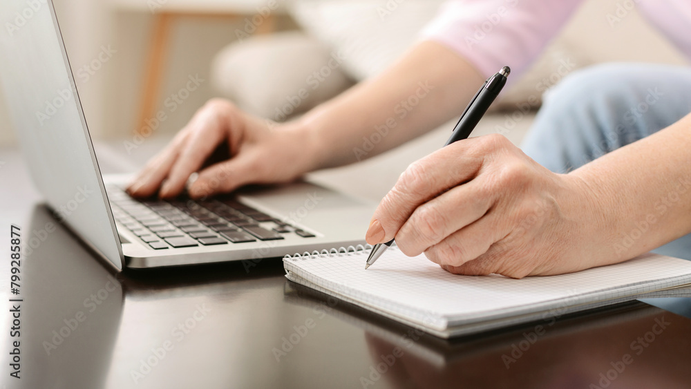 Senior woman writing down thoughts and working on laptop Senior woman writing down thoughts and working on laptop