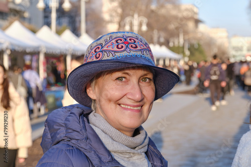 Portrait of senior Caucasian woman, wearing felt hat with Kazakh embroidered pattern, at crafts fair