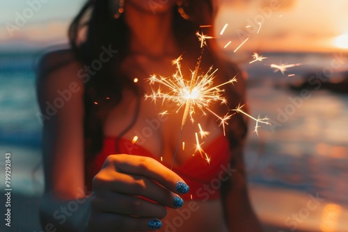 A woman holding a sparkler, wearing blue glitter nails and a red dress with a blurry background