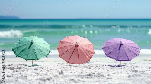 3 green, pink and purple cocktail umbrellas on the beach with white sand, ocean in the background. © Image