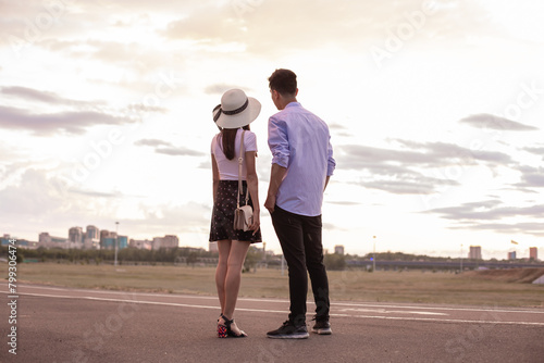 The guy and the girl stand with their backs to the camera and look into the distance