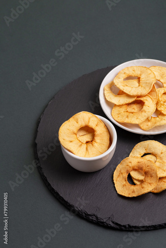 Apple chips in a white plates on a blackstone desk on a dark background.