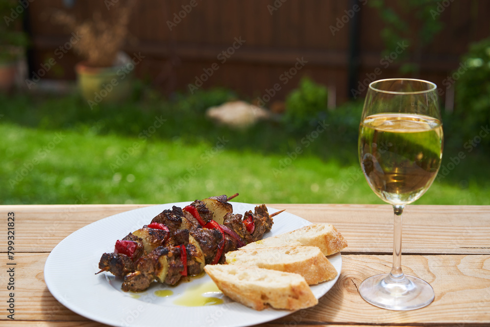 Grilled greek style lamb skewer with rustic wheat bread and sparkled by extra virgin olive oil and glass of white wine, served outside. Ideal and tasty dish for summer party with family or friends.