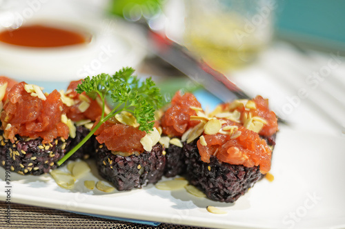 Japanese sushi with black rice, spicy tuna, almonds, sesame seeds and parsley on white plate. Selective focus