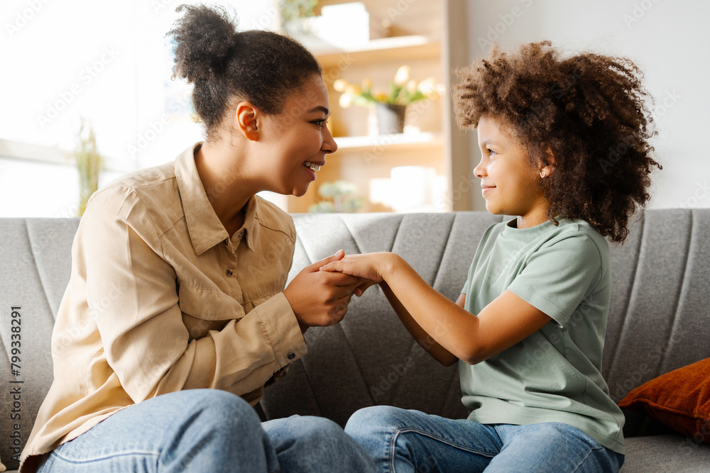 Happy pretty mother looking at her little daughter while holding her hands, sitting on sofa at home Happy pretty mother looking at her little daughter while holding her hands, sitting on sofa at home