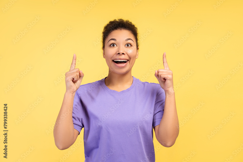 Young African American woman amazed and surprised looking up, pointing with fingers and raised arms Young African American woman amazed and surprised looking up, pointing with fingers and raised arms