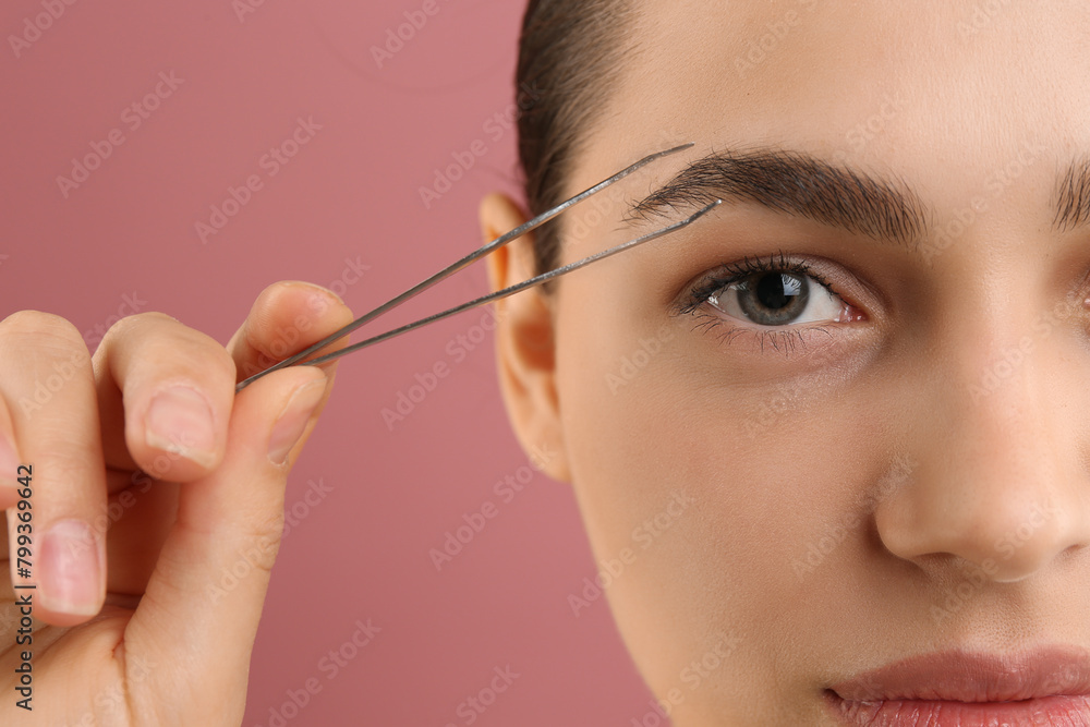 Obraz premium Eyebrow correction. Young woman with tweezers on pink background, closeup