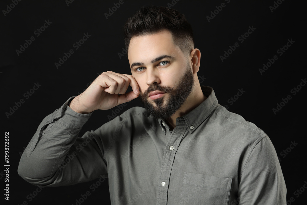 Young man in shirt touching mustache on black background Young man in shirt touching mustache on black background