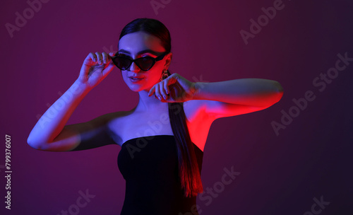 Portrait of beautiful young woman in sunglasses on color background with neon lights