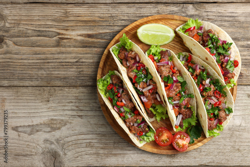Delicious tacos with meat, vegetables and lime on wooden table, top view. Space for text