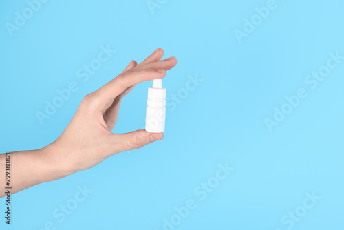 Woman with bottle of medical drops on light blue background, closeup