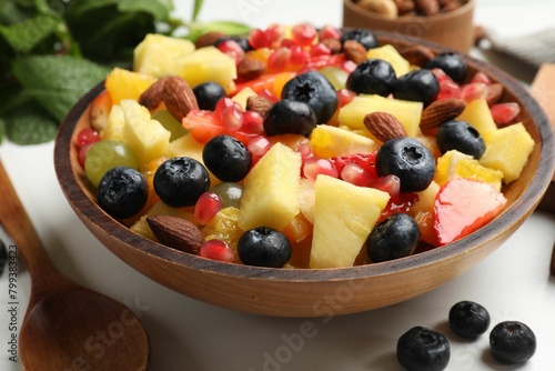 Delicious fruit salad in bowl  berries  fresh mint and nuts on white marble table  closeup
