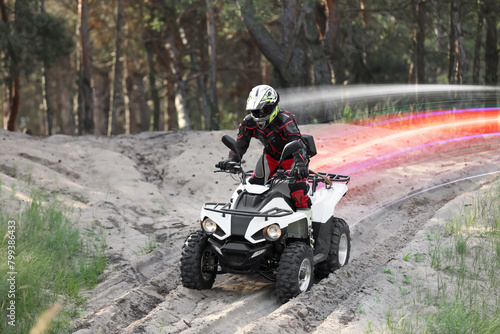 Man driving modern quad bike on sandy road near forest. Light trails showing his speed