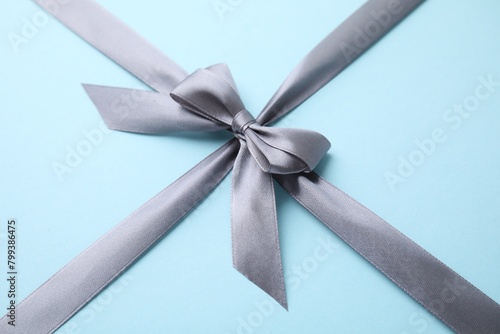 Grey satin ribbon with bow on light blue background, closeup