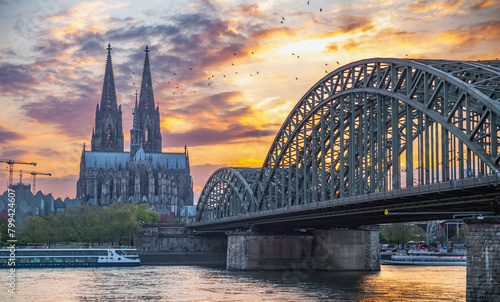 the Cologne Cathedral and Hohenzollern Bridge at sunset with birds flying in the sky photo