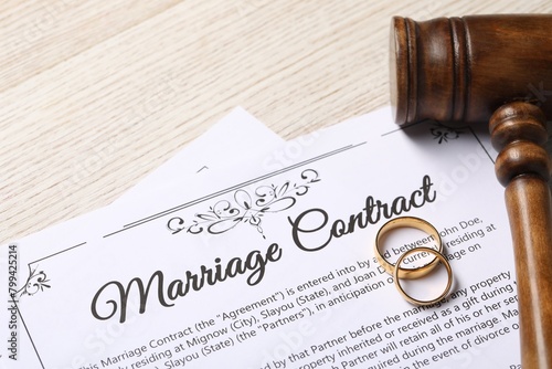 Marriage contract, golden wedding rings and gavel on wooden table, closeup
