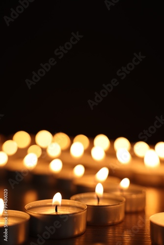 Burning candles on dark surface against black background, closeup. Space for text