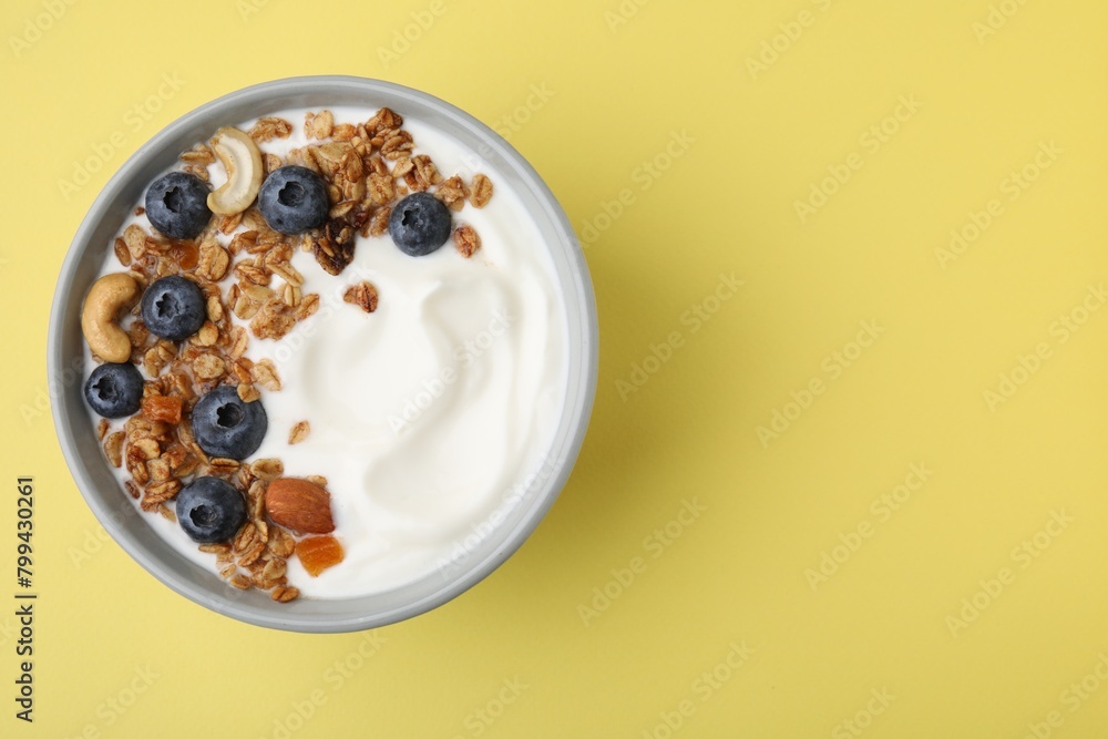 Fototapeta premium Bowl with yogurt, blueberries and granola on yellow background, top view. Space for text