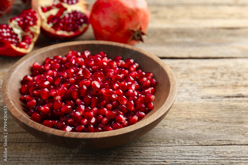 Ripe juicy pomegranate grains in bowl on wooden table. Space for text Ripe juicy pomegranate grains in bowl on wooden table. Space for text