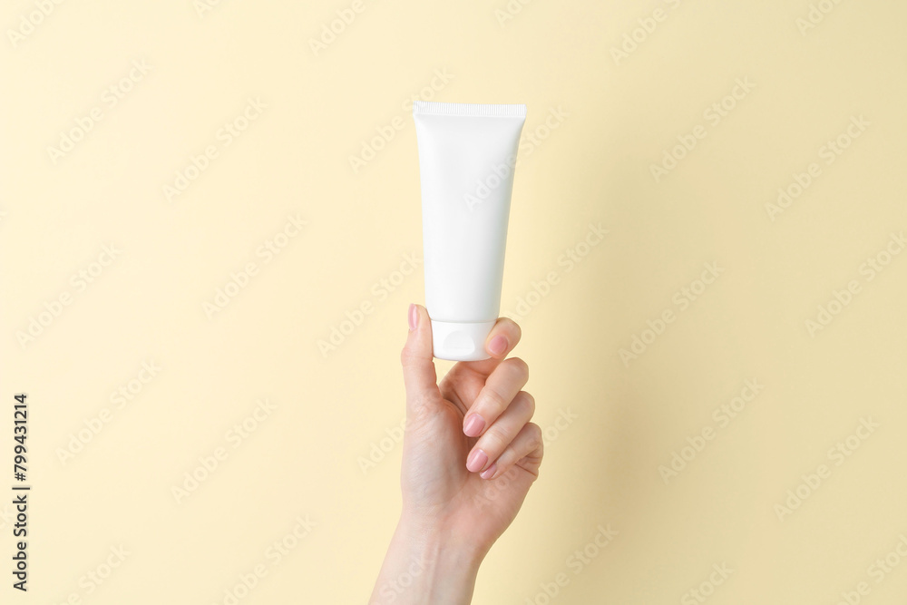 Woman holding tube of cream on yellow background, closeup Woman holding tube of cream on yellow background, closeup