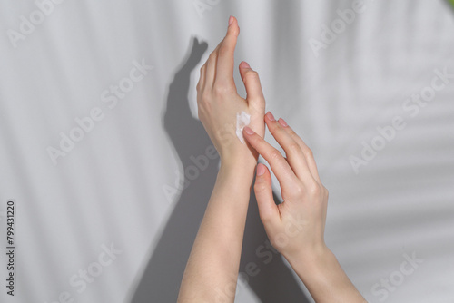 Woman applying cream on her hand against grey background, closeup
