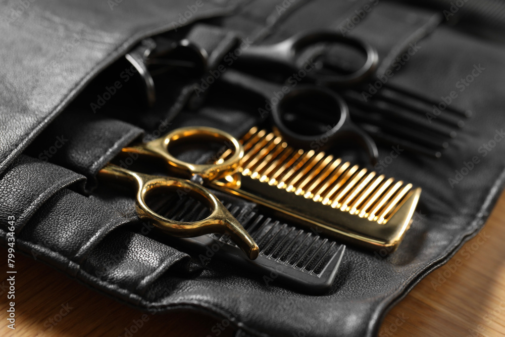 Hairdresser tools. Professional scissors and combs in leather organizer on wooden table, closeup Hairdresser tools. Professional scissors and combs in leather organizer on wooden table, closeup