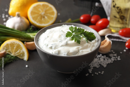 Delicious yogurt in bowl and ingredients on black table, closeup
