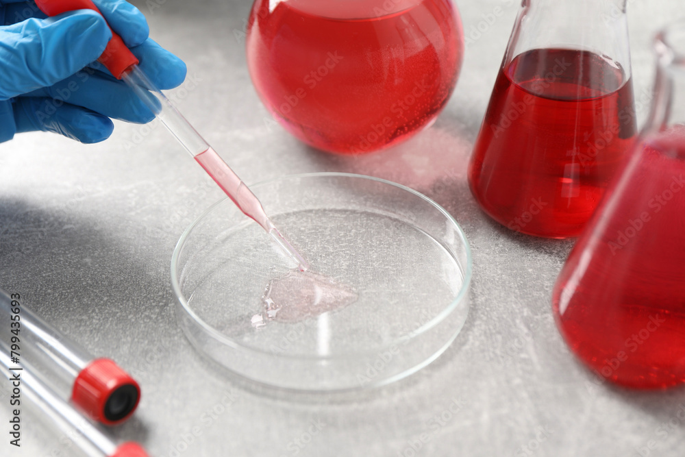 Laboratory analysis. Dripping red liquid into Petri dish on light grey table, closeup Laboratory analysis. Dripping red liquid into Petri dish on light grey table, closeup