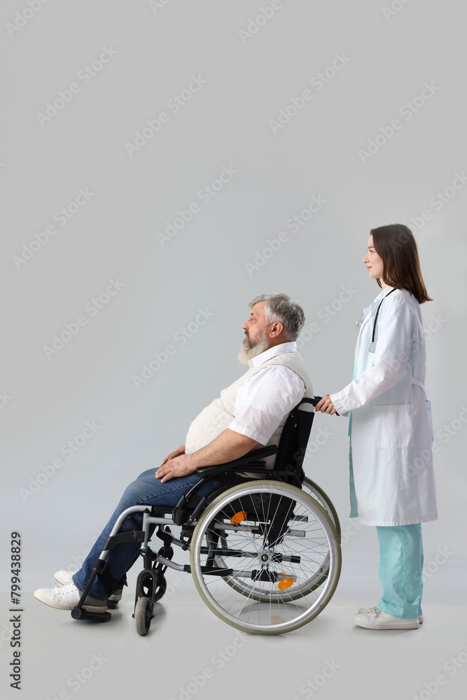 Mature man in wheelchair with nurse on light background Mature man in wheelchair with nurse on light background