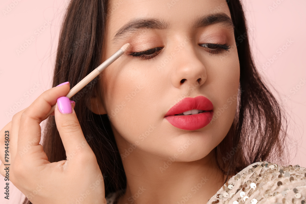 Beautiful young woman with brush applying eyeshadows on pink background Beautiful young woman with brush applying eyeshadows on pink background