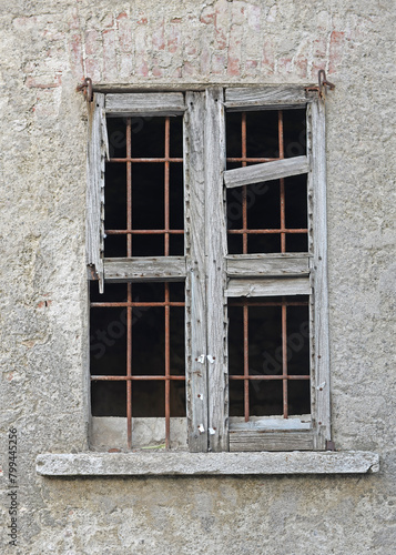 Old, broken, rotten window with rusty bars in weathered plastered brick wall