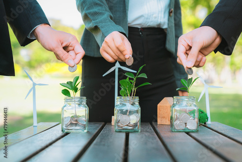 Business people put coin to money saving glass jar on outdoor table as sustainable money growth investment or eco-subsidize. Green corporate promot and invest in environmental awareness. Gyre photo