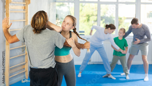 Purposeful engrossed teen girl train during krav maga training session and work out basic elements with male partner. Martial arts school, melee