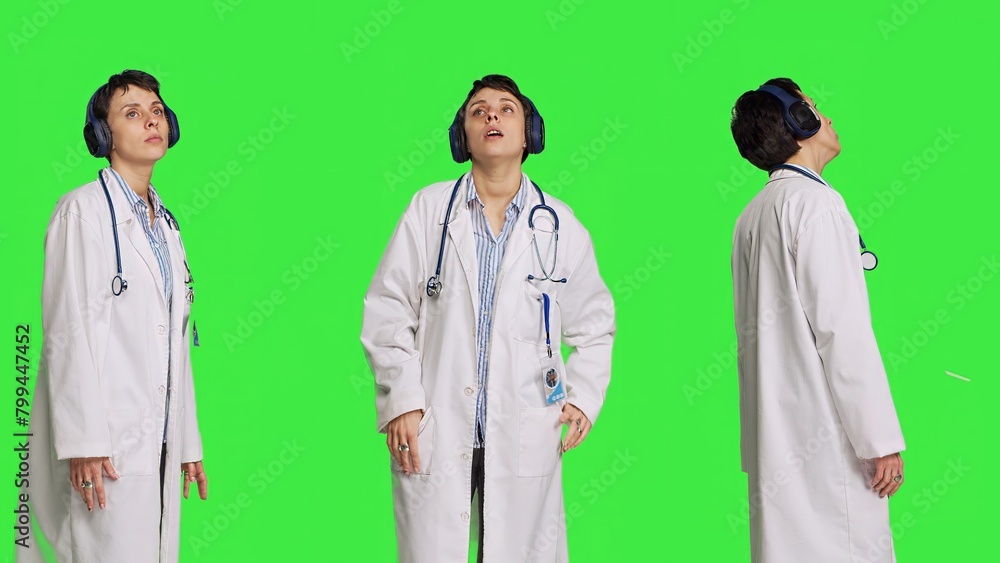 Joyful physician dancing around in the studio with music on headset, having fun with modern cool songs against greenscreen backdrop. Medic woman enjoying audio tunes and singing. Camera B.