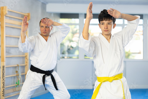 Dynamic underage boy performing fighting positions with middle-aged trainer during karate courses